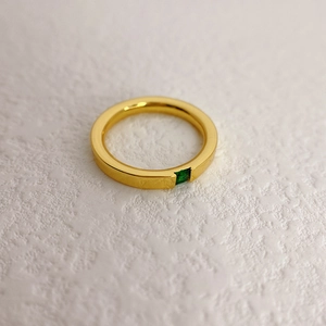 Nahaufnahme von minimalistischem vergoldetem Ring mit quadratischem grünem Edelstein