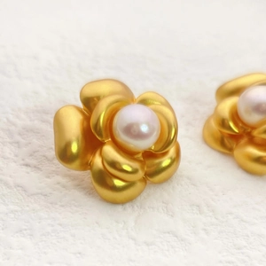 Detailed close-up of matte gold camellia flower earrings with a central pearl inlay