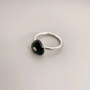 Makro-Detail des silbernen Rings mit schwarzem Emaille-Herz auf grauem Hintergrund
