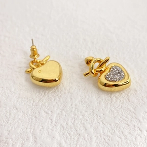Minimalist heart-shaped gold studs with pavé rhinestones and knot detail on white background