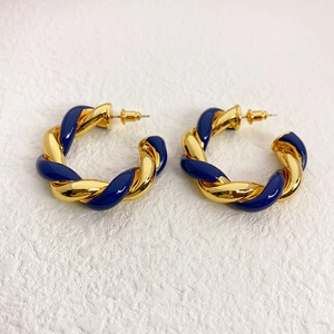 Detail of gold and dark blue enamel twisted spiral C-shape hoop earrings on white background