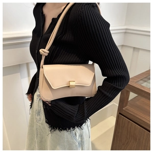 Detail of beige shoulder bag featuring golden clasp and decorative knotted strap detail