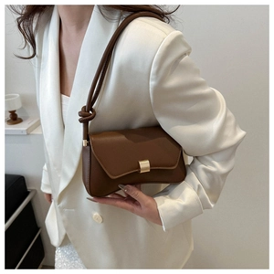 Detail of a deep brown leather shoulder bag with a gold buckle on a white satin blazer