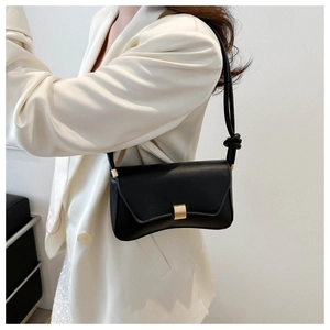 Detail view of black leather underarm bag featuring a gold lock and knotted strap detail