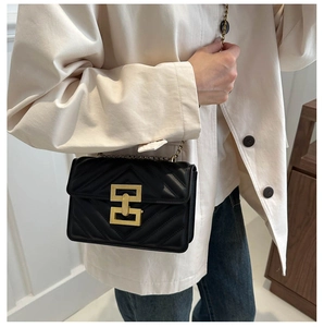Detail of a black quilted crossbody bag with a gold rectangular metal buckle clasp