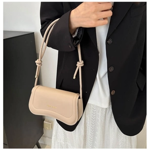 Detail of beige PU leather shoulder bag with wavy bottom and knot strap on a model