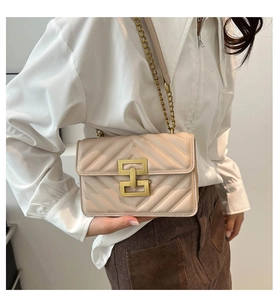Close-up of beige quilted shoulder bag with V-shaped stitching and gold geometric clasp