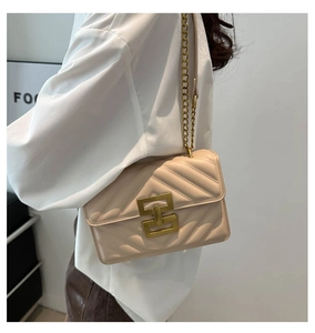 Close-up of beige quilted crossbody bag featuring golden lock and chain strap details