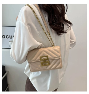 Detail of beige quilted flap bag with V-shaped stitching and golden chain strap on model