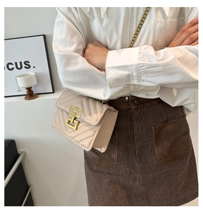 Detail of a beige quilted crossbody bag with golden geometric lock on a female model