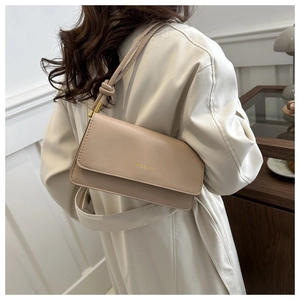 Model wearing a minimalist beige crossbody bag with gold logo on a white coat