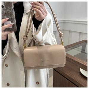 Detail of beige square shoulder bag with gold lettering and decorative knot strap