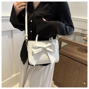 White PU bucket bag with large bow detail shown carried by a model in casual outfit