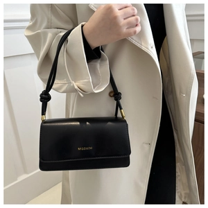 Detail of a black leather crossbody bag with gold lettering and tied strap knots