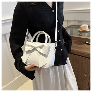 Close-up of white bow bucket bag with smooth leather finish and stylish shoulder strap