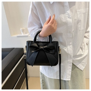 Detail of black bow bucket bag with gold hardware and adjustable crossbody strap