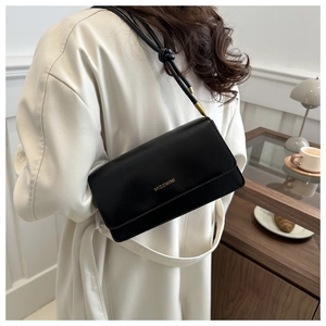 Minimalist black rectangle crossbody bag with gold logo on white coat model