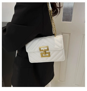Close-up of white quilted crossbody bag with gold geometric metal lock on a black suit