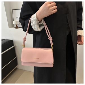 Pink leather shoulder bag detail showing knotted strap and gold logo against a black coat