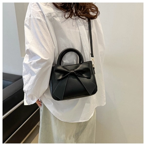 Detail of a chic black PU leather handbag with a large bow decoration worn by a model