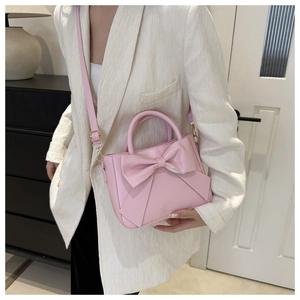 Detailed view of pink leather handbag with bow detail worn with white striped suit