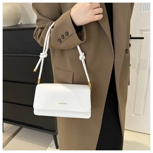 Detail of white minimalist crossbody bag with gold hardware and rope strap knot