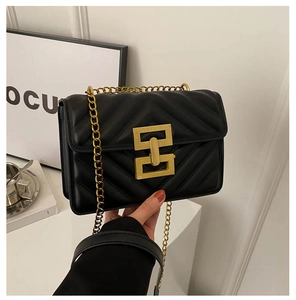 Detail of black quilted shoulder bag with V-shaped stitching and gold chain strap