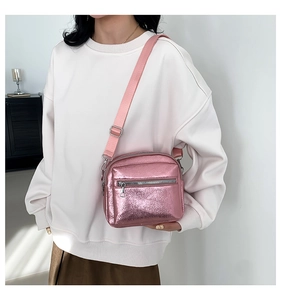 Detalle de un bolso bandolera rosa metálico brillante con textura y correa ajustable