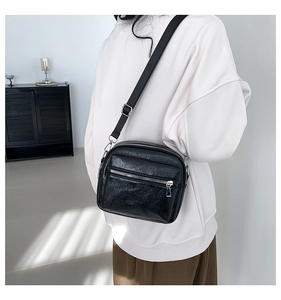 Detalle de bolso bandolera negro minimalista con textura brillante y doble cremallera