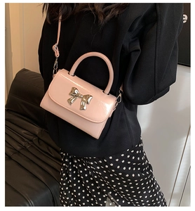 Detail of pink patent leather handbag featuring a decorative silver metal bow on the front