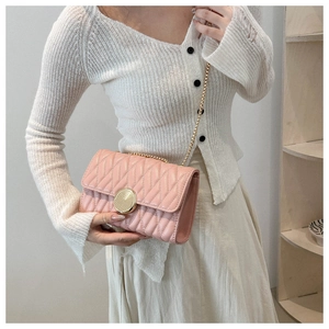 Gros plan du sac à chaîne matelassé rose avec fermoir doré sur une tenue beige
