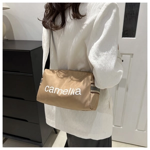 Close-up of khaki nylon shoulder bag featuring white Camellia lettering and striped strap