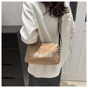 Detailed view of camel nylon crossbody bag with camellia lettering and striped strap