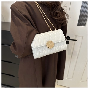 Détail de la texture matelassée blanche et du fermoir doré rotatif sur un sac à bandoulière