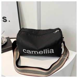 Detail of black nylon cylinder bag with white camellia lettering and striped strap
