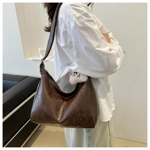 Detail of dark brown PU hobo bag with vintage texture and white plush decor charm