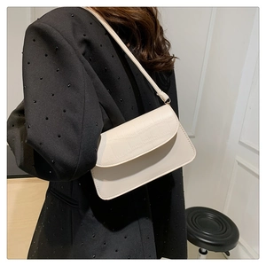Detail view of stylish cream shoulder bag with crocodile pattern flap on minimal white wall