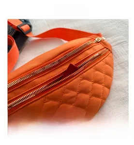 Detail of orange quilted waist bag featuring dual gold zippers and storage for small items