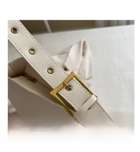 Detail of adjustable PU leather strap with gold eyelets and buckle on beige crossbody bag