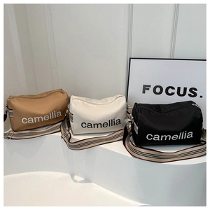 Three nylon cylinder crossbody bags in khaki, cream, and black with striped straps