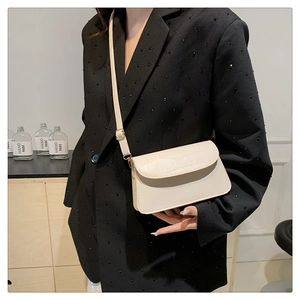Detail of a creamy white crossbody bag with crocodile embossed flap and adjustable strap