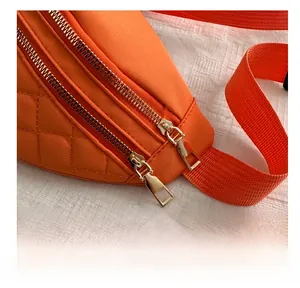 Detail of orange quilted waist bag featuring gold double metal zippers and nylon strap