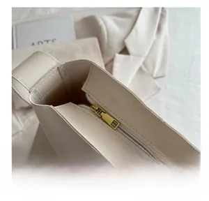 Close-up of smooth gold metal zipper closure on minimalist cream bucket bag texture