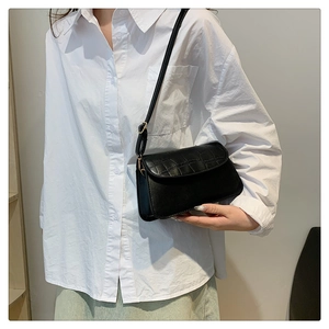 Detail of black crossbody bag with faux crocodile texture and gold hardware on white shirt