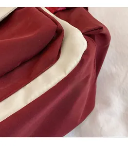 Detailopname van contraststiksels en geweven textuur op de bordeaux canvas tas