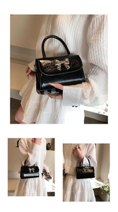 Close-up of black glossy pleated handbag featuring a prominent gold bow metal clasp
