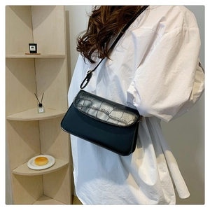 Detail view of black crocodile-embossed crossbody bag worn on white shirt outfit