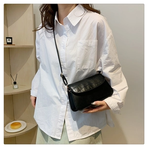Detail of black crossbody bag with crocodile texture flap and golden hardware on a model