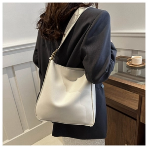 Close-up of minimalist cream leather bucket bag showing soft texture and wide shoulder strap