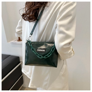 Dark green glossy shoulder bag with chunky chain and FASHION label on white blazer